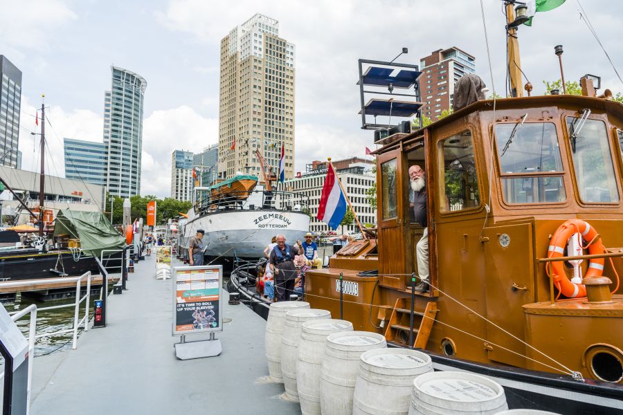 Outside view of the Maritime Museum Rotterdam and Museumhaven featuring historic ships docked along the quay, with the museum building and city skyline in the background

