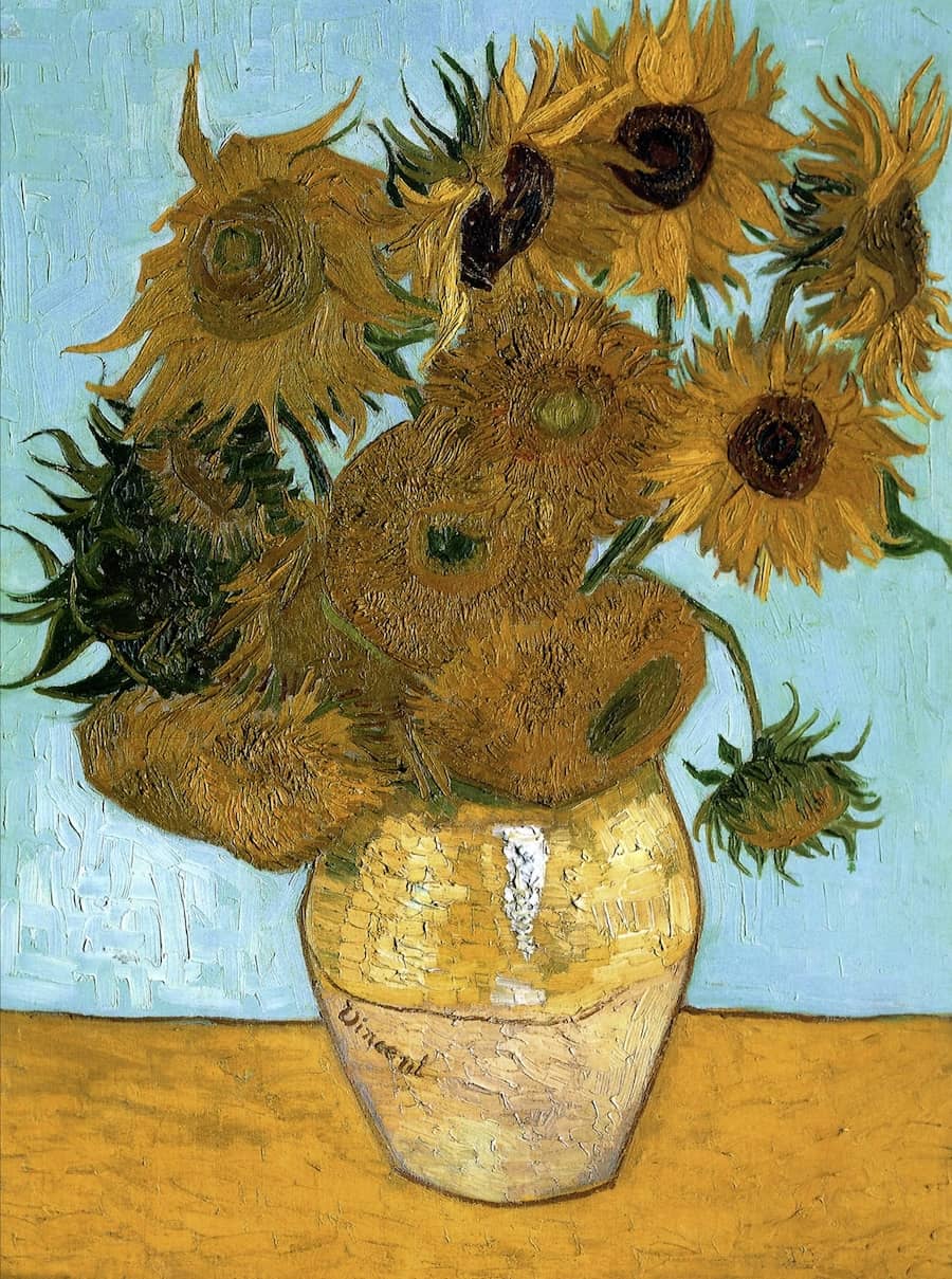 A still life painting of a yellow vase filled with twelve vibrant sunflowers, set against a golden-yellow background. The flowers vary in stages of bloom, with some fully open and others drooping. Thick, expressive brushstrokes give the petals and stems a textured, lively appearance, characteristic of Van Gogh’s signature post-impressionist style.